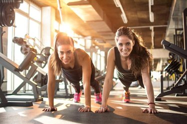 Two sporty girls doing push ups in gym.