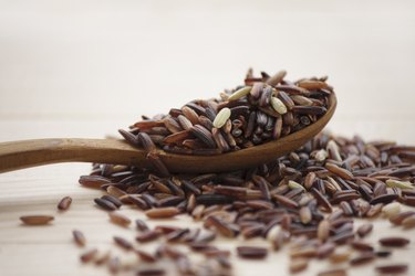 Wooden spoon overflowing with dry wild rice grains on a wooden tabletop