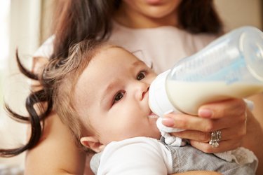 Mother Feeding Baby Boy From Bottle At Home