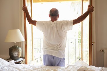 Rear View Of Man Waking Up In Bed In Morning