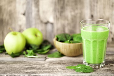 green smoothie juice on wooden table with spinach and apples