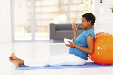 pregnant african american woman eating healthy salad on exercise mat