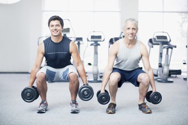 Men doing squats with dumbbells in gymnasium