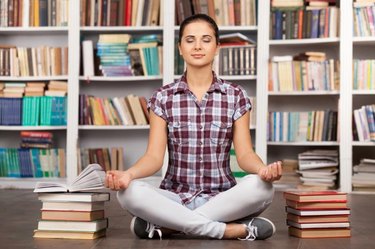 Beautiful young woman keeping her eyes closed and meditating while sitting at the library