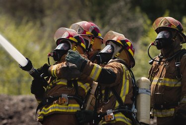 a group of firefighters in full gear dowse a fire with a firehose