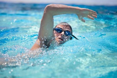 Young man swimming the front crawl in a pool, wearing swimming glasses