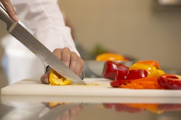 Female chef slicing peppers on chopping board, close-up