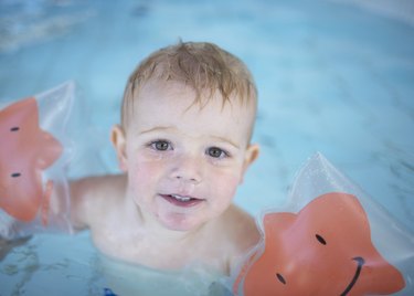Boy (18-21 months) wearing armbands in swimming pool, portrait