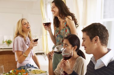 Three young women and young man drinking red wine, two women laughing