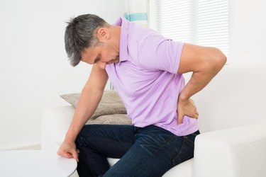 Mature Man Having Backache While Sitting On Sofa