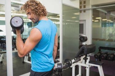 Handsome young man exercising with dumbbell in gym