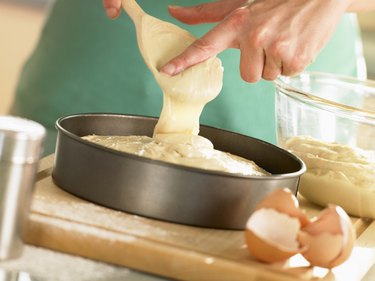 person pouring mixed cake mix with vegetable oil substitution into round pan with eggshells