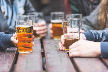 Hands holding glasses with beer on a table at a pub.