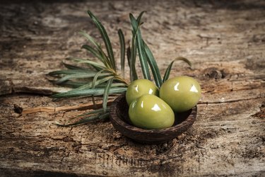Olives with leaves on a wooden surface.