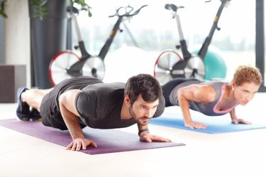 Portrait of personal trainer woman and man doing push ups at the gym.