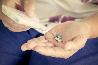 old woman hand pouring pills from a pill reminder box