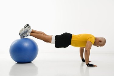 Side view of mid adult multiethnic man doing pushups while balancing on blue exercise ball.