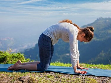 Yoga exercise outdoors - sporty fit woman practices yoga asana Marjariasana - cat pose outdoors in Himalayas