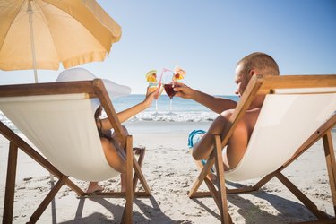 Happy couple clinking their glasses while relaxing on their deck chairs