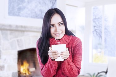Attractive girl warming at fireplace hold coffee