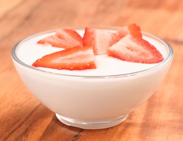 full bowl of yogurt with strawberries on wood