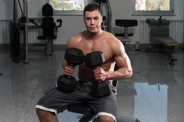 Young Man In Gym Exercising Chest With Dumbbells