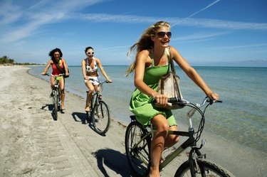 Three young women riding bicycles on beach, smiling