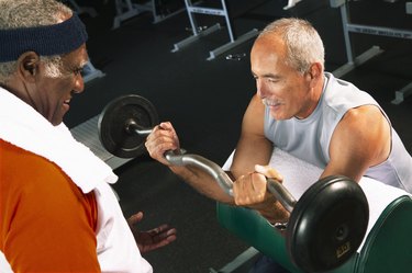 Senior man helping mature man weight train in gym