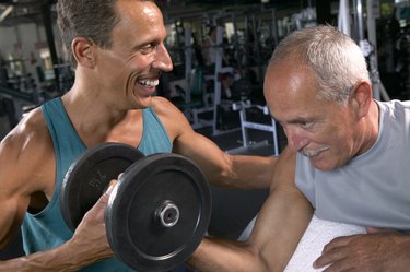 Two mature men in gym, one lifting weights