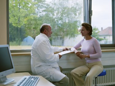 Male doctor sitting with female patient by window, smiling