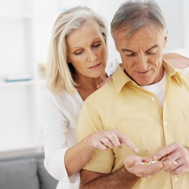 Close-up of mature man holding pills and mature woman looking at pills
