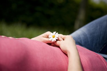 A woman lying on the grass, holding a daisy, cropped