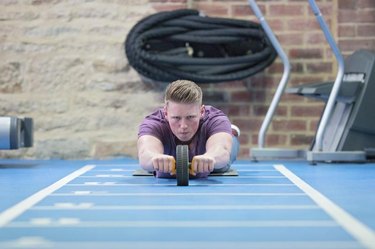 Young man training his abs on the ab roller in the gym.