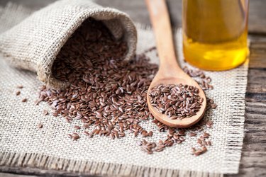 Flax seeds in the sack and oli on wooden background