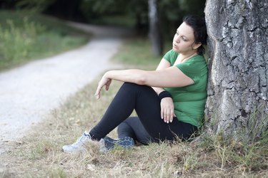Tired overweight woman sitting by the tree