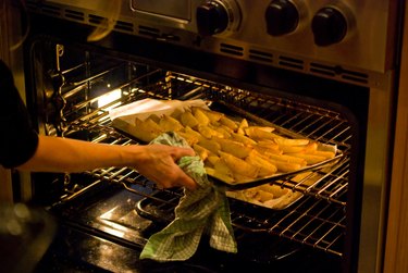 Woman lifting a tray of potato wedges into oven