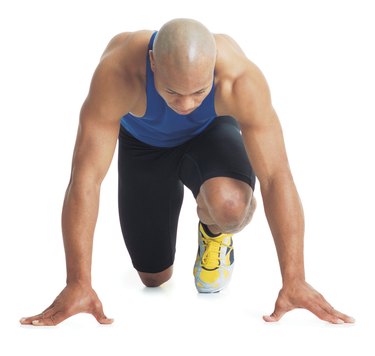 a young bald black male runner wears a blue tank top and leans forward in the starting position