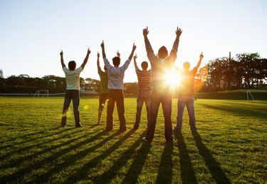 Group of men in park, outstretching arms against sun, rear view