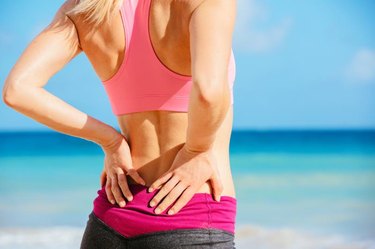 Back Pain. Athletic fitness woman rubbing the muscles of her lower back. Sports exercising injury.