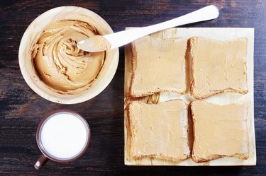 Sandwiches with peanut butter on wooden plate, peanut butter in