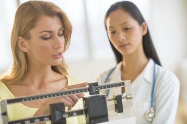 Woman Adjusting Weight Scale While Standing By Female Doctor