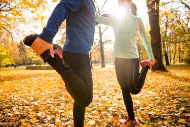 Detail of man and woman stretching legs before jogging in autumn nature
