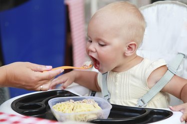 Little Caucasian baby eats with help of mother