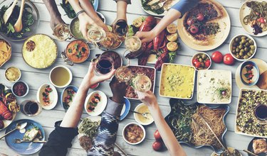 photo of a large dining table from above with hands clinking glasses over a spread of many dishes of food