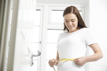 Happy Teenage Girl Measuring Waist In Bathroom