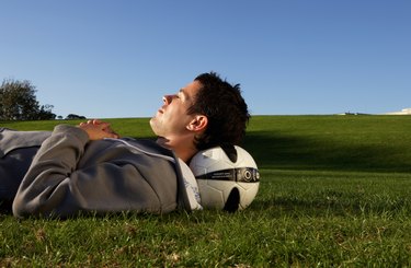 Young man lying in field with football under head, profile