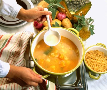 close-up of a hand stirring a bowl of soup cooking on a stove