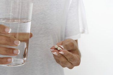 Woman holding pills and glass of water, mid section
