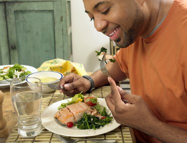 Man Sits at a Table at Home Eating a Salmon Salad for Lunch