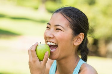 欢快的年轻女子在公园吃苹果